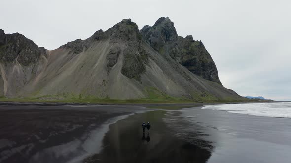 Drone Of Men Walking Along Black Beach To Vestrahorn Mountain alt