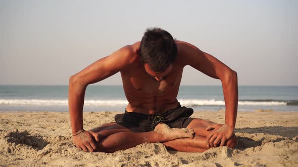 A Young Man Practices Yoga Outdoors Against the Background of the Sea alt