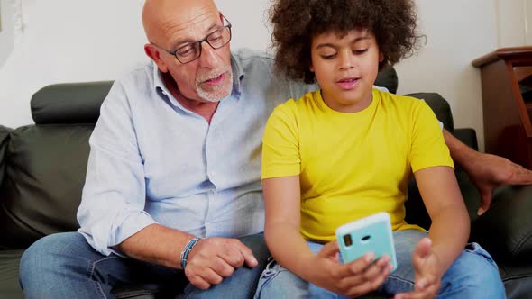 Grandson and grandfather sitting on couch using smartphone alt
