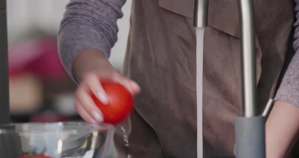 A Woman Washes Tomatoes Under a Stream of Water From a Tap alt