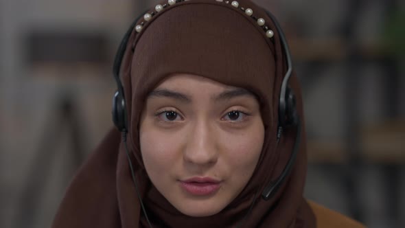 Headshot Portrait of Young Confident Middle Eastern Woman in Headphones and Hijab Talking Looking at alt