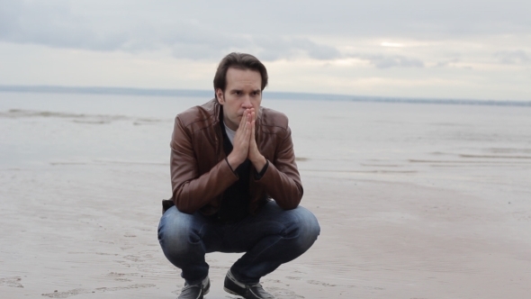 Young Man Crouching By The Sea