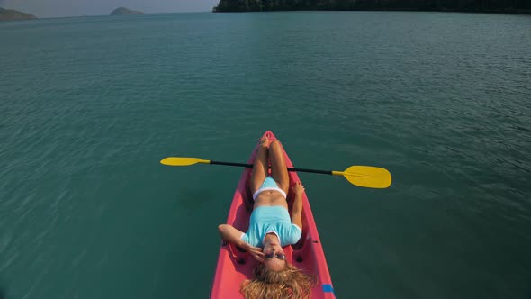 Pretty Slim Woman in Elegant Swimsuit Lies in Pink Plastic Kayak Drifting on Azure Ocean at Exotic alt