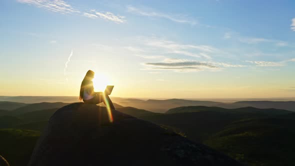 Young Attractive Woman Typing on a Laptop on a Mountaintop at Sunset