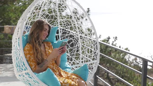 Beautiful Woman on the Balcony in a Swing Against the Backdrop of a Beautiful Landscape alt