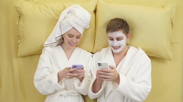 Positive Married Couple Enjoying Weekends Having Rest on Bed and Using Smartphone