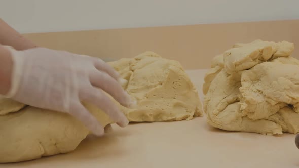 Woman Baker's Hands in White Gloves Knead Dough From Pieces of Blanks Which Lie Next To Each Other alt