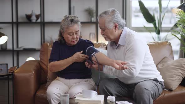 Asian elderly couple using a blood pressure monitor to the wife in the house