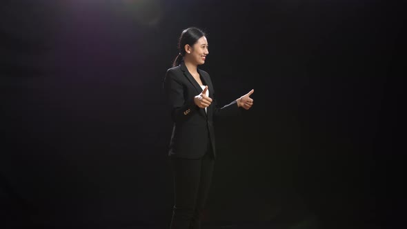 Smiling Asian Speaker Woman In Business Suit Showing Thumbs Up Gesture In The Black Screen Studio alt