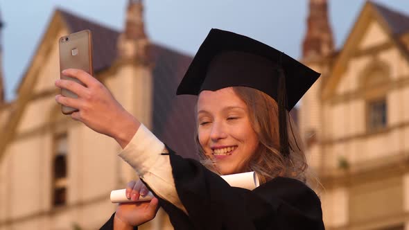 Attractive Graduate Girl Taking Selfie on Graduation Day Holding Diploma alt