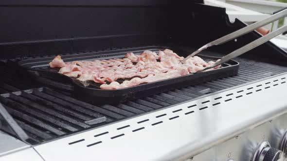 Cooking bacon stips on an outdoor gas grill. alt