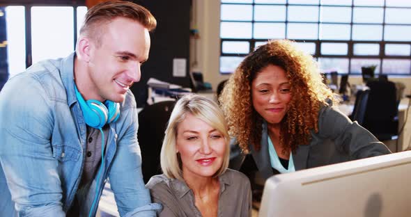Businesswoman interacting with coworkers while working on computer alt