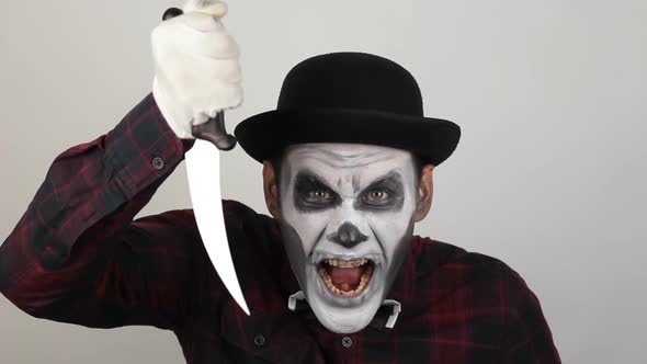 A Horrible Man in Clown Makeup Threatens His Victim with a Sharp Knife. The Scary Clown Looks at the