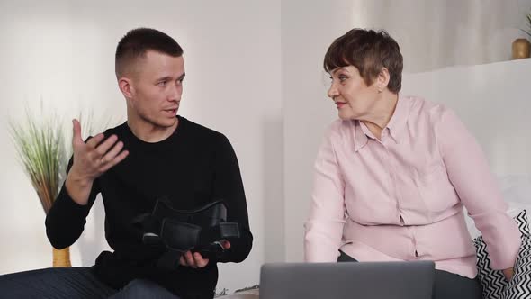 Joyful Grandson Is Talking and Showing To Senior Woman How To Use Vr Glasses