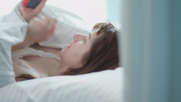 Woman Puts Her Head on a Pillow in the Bed in the Morning and Uses the Phone Reading Some