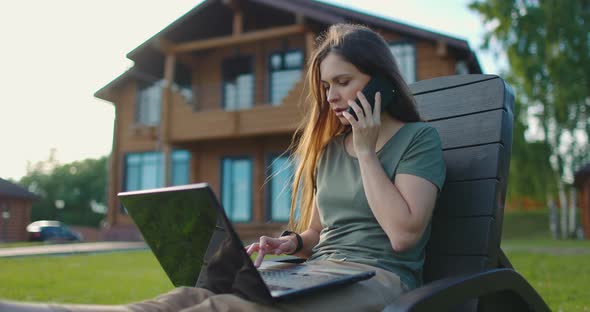 Young Woman Works on Laptop Sitting in Courtyard of Country House alt