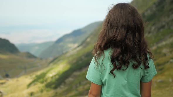 Cinematic back view of a girl looking out over a green valley of mountains.