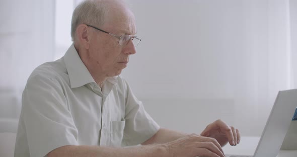 Aged Gray Man with Glasses Is Working with Notebook, Surfing Internet and Chatting Online By alt
