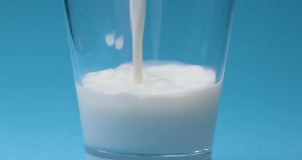 Milk is poured into a milk glass on a blue background. alt