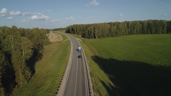 The Drone Follows a Car and a Truck Over a Road Where Cars Move in the Stream
