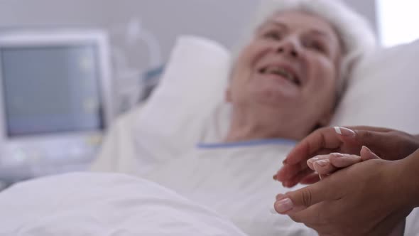 Senior Lady Holding Hands with Nurse in Hospital Ward alt