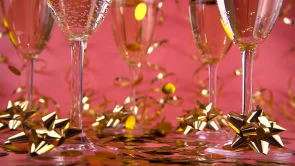 Falling confetti on glasses with sparkling wine on a pink background with serpentine. Slow motion. alt