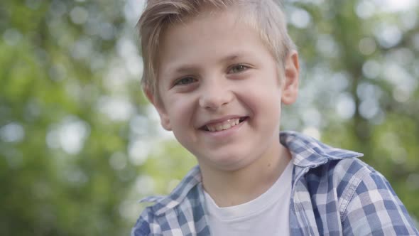 Close-up Portrait of Cute Handsome Boy in Checkered Shirt Looking Into Camera Sitting in the Park alt