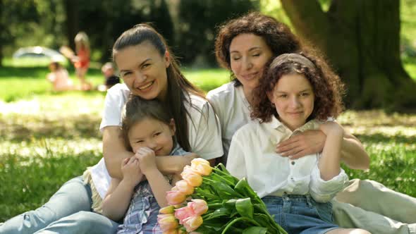 Two Women with Their Daughters are Sitting in the Park on the Grass
