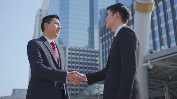 Asian businessmen making handshake after complete the negotiation. Business deal, merger in city. alt