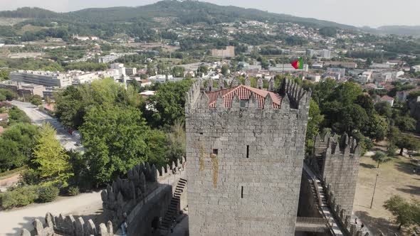Portuguese flag flapping on tower at medieval Guimaraes Castle; drone pan