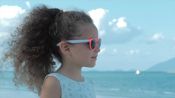 Close-up Portrait of a Beautiful Little Girl in Pink Glasses, Cute Smiling, Looking at the Sea alt