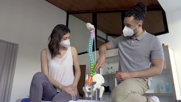 Physiotherapist discussing spine and hip model with female patient alt