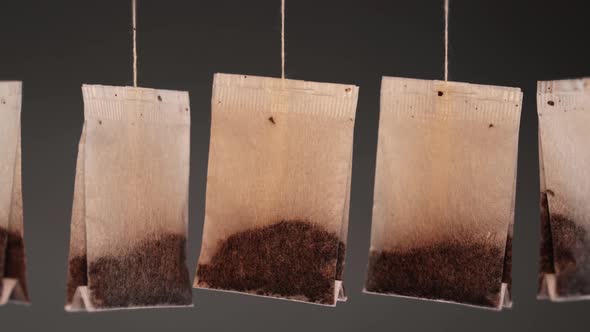 Tea Bags on Threads Hang Waved By Wind on Dark Background alt