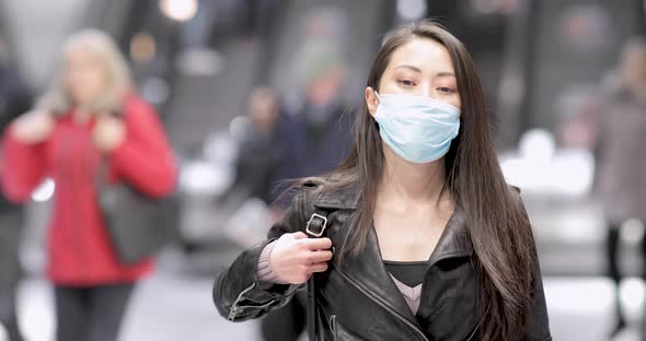 Chinese woman at train station in London wearing face mask to protect from co alt