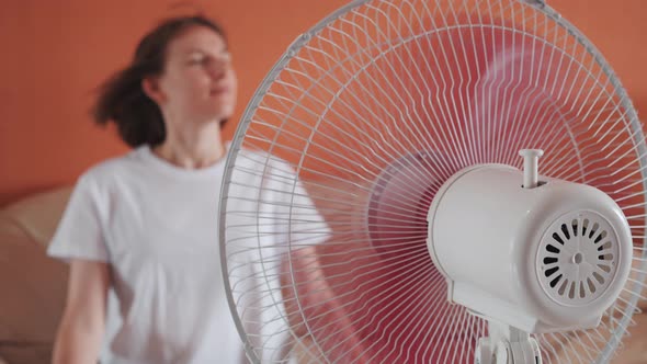 Young Woman Sits in Front of Electric Home Fan Air Stream Blowing Short Hair alt