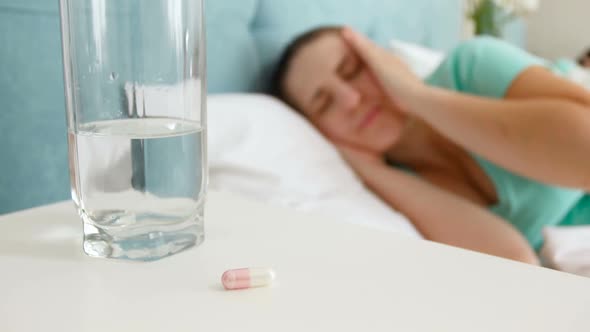 Footage of Young Sick Woman Lying in Bed Taking Pill From Bedside Table and Drinking It with Glass alt