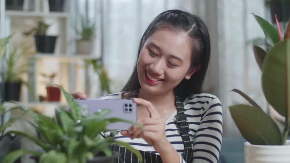 Close Up Of Smiling Asian Woman Holding Smartphone And Taking Photos Of Plants At Home alt