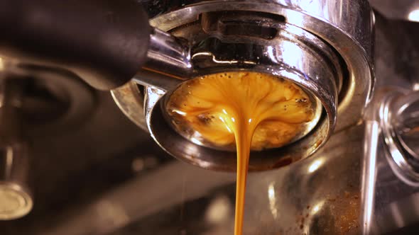 Closeup of pouring coffee stream from professional machine through the bottomless portafilter type alt