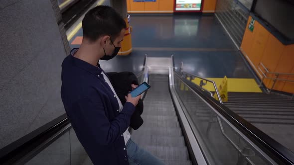 Unrecognizable man surfing internet on smartphone on escalator in underground alt