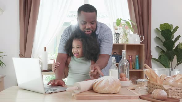 Black father and little daughter watching class online with laptop at the home kitchen table
