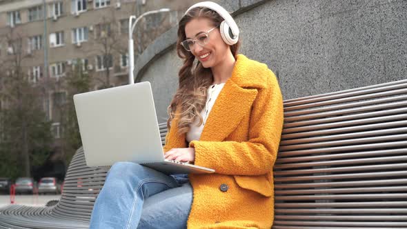 Business Woman Wear Eyeglasses Listen Music Headphone Outdoor Sitting Bench Using Laptop Outdoor alt