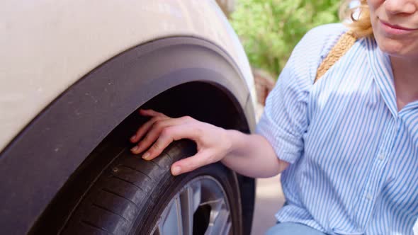 the Woman Inspects the Puncture Site on the Flat Tire of the Car alt