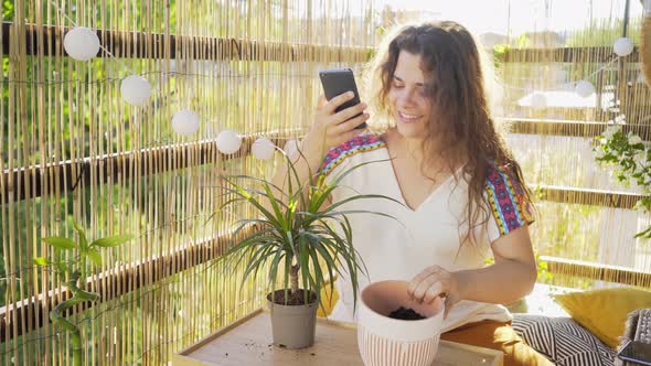 Smiling Female Takes Photo with Plant on Balcony