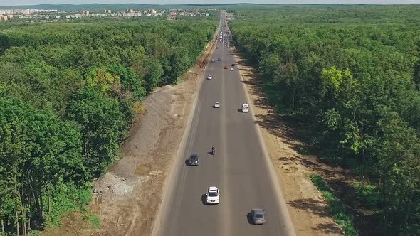 Drone Is Flying Over Long Straight Highway Through Dense Forest, in Sunny Summer Day