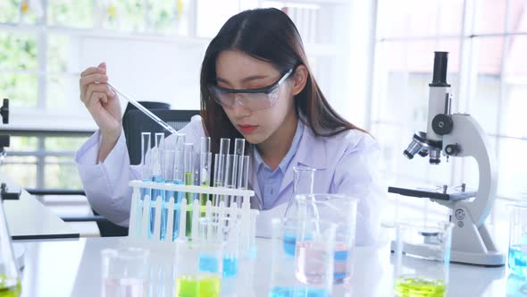 Asian Medical Researcher Working in Pharmacy Laboratory While Mixing Chemical in Flask with Tube alt