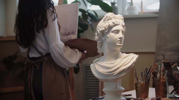 Young Woman Artist with Long Hair Drawing a Painting  Marble Bust on the Foreground alt