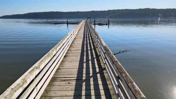 Flying through wood dock pier, danger sign over bright blue water, distant green trees ocean coast alt
