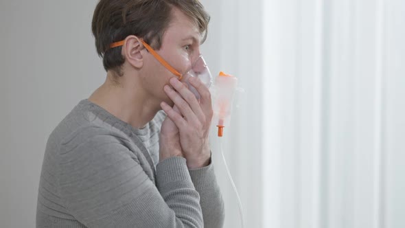 Side View of Concentrated Brunette Caucasian Man Inhaling and Exhaling Using Inhaler alt