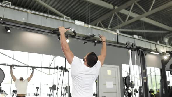 A Strong Caucasian Man Dressed in Workout Clothes Does Reps on the Pulldown Equipment in a Gym