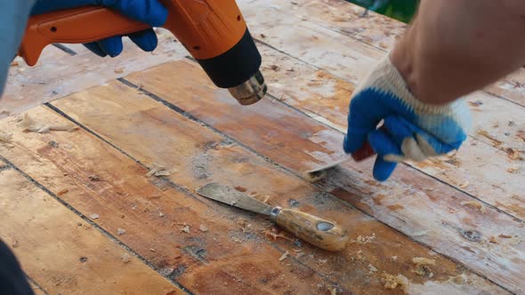 Man Removing Old Varnish From Wood Using Scraper and Heat Gun alt